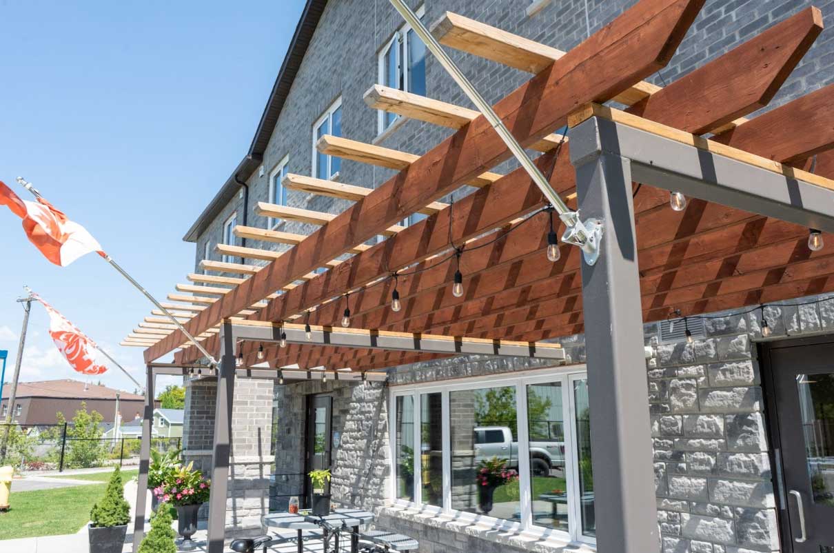 A modern building with gray brick siding and a large wooden pergola.